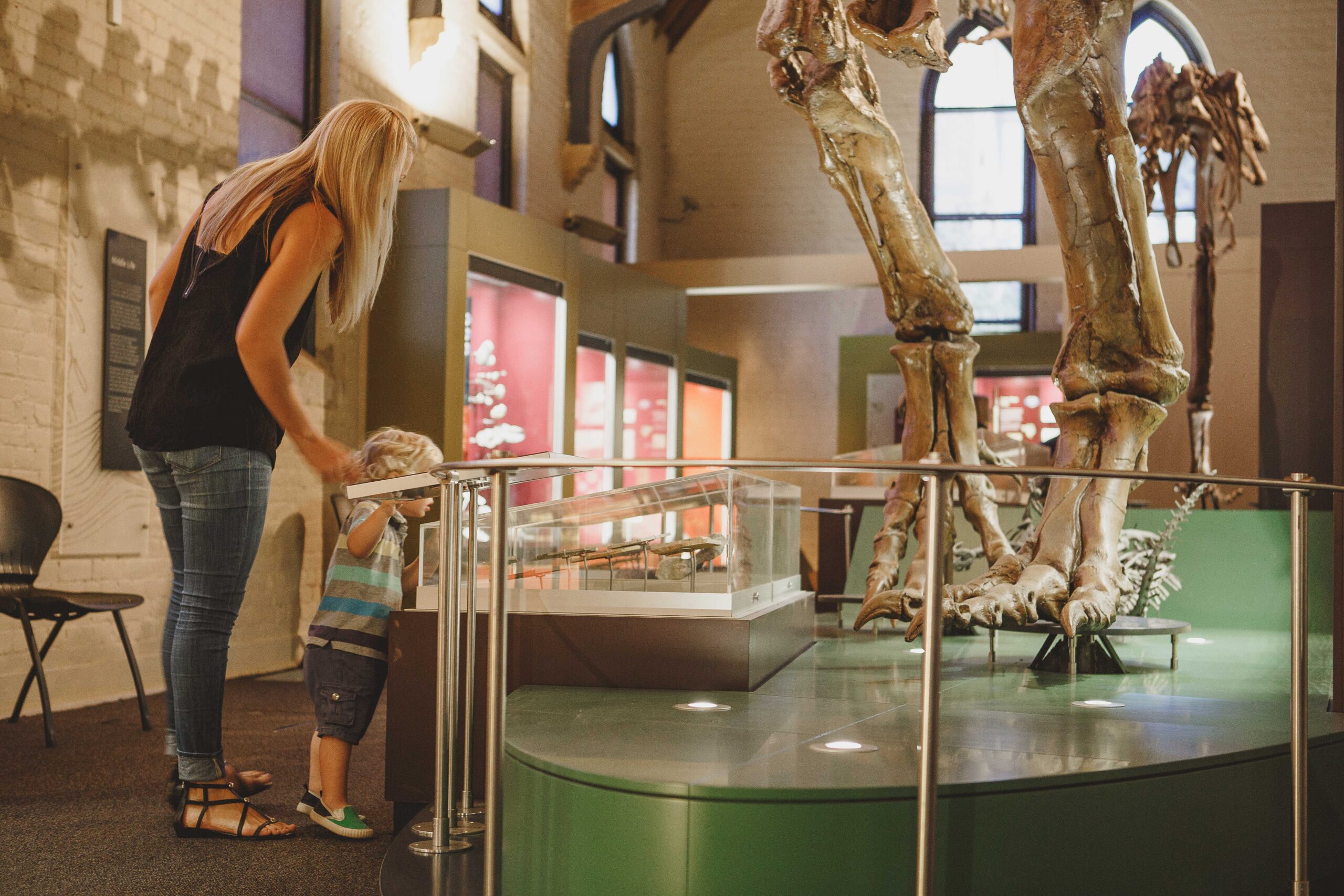 parent and their child look at the legs of a large dinosaur fossil