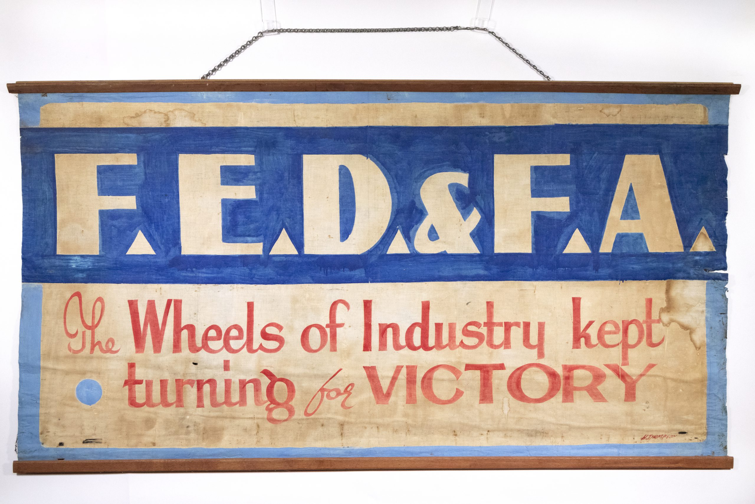 blue, white, and red lettered banner which says 'F.E.D.& F.A. / The Wheels of Industry kept turning for VICTORY'