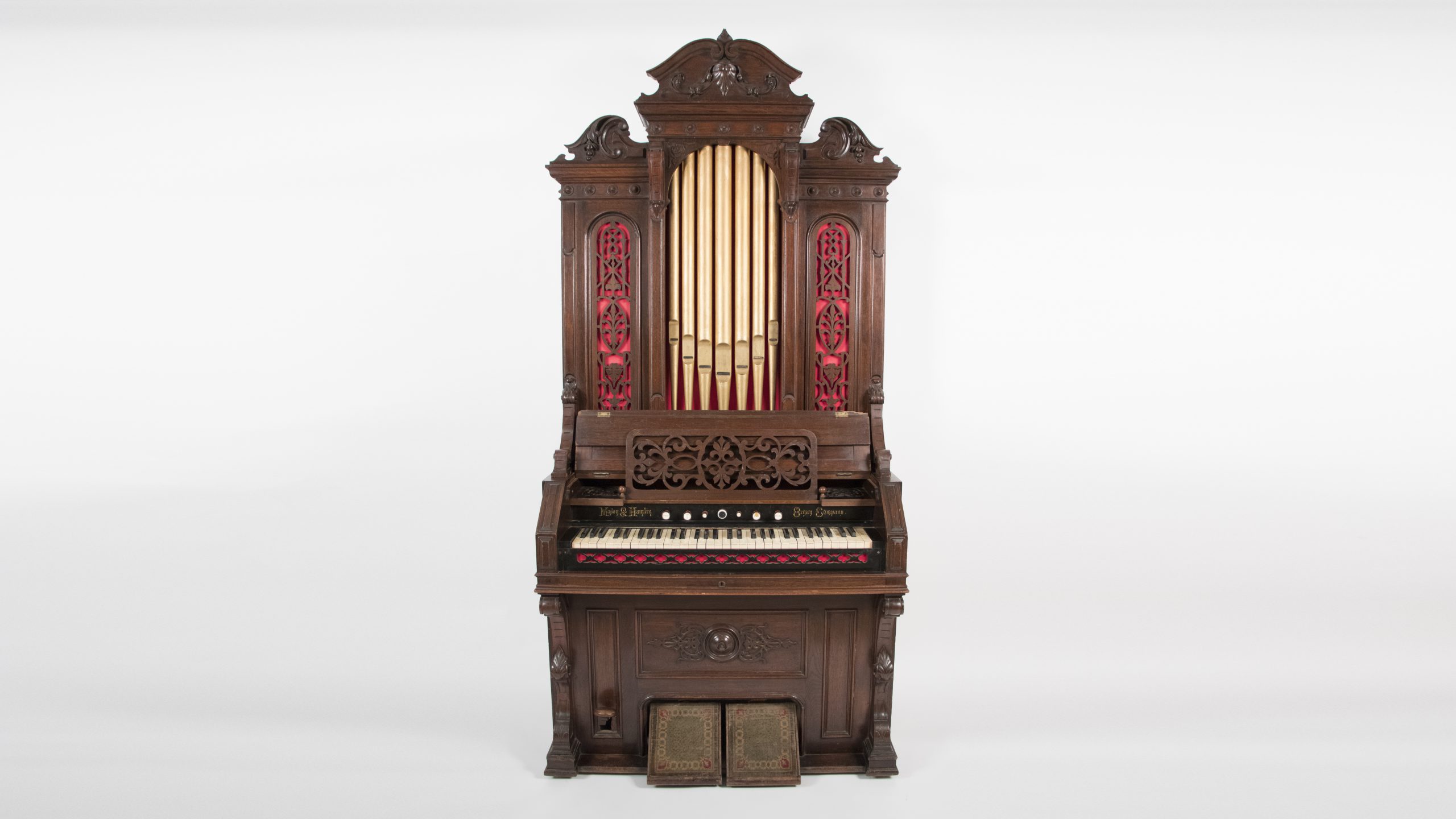 grand, pipe organ, it has tall wooden case with central metal pipes, either side of the pipes are red decorative panels with wooden designs overlaid
