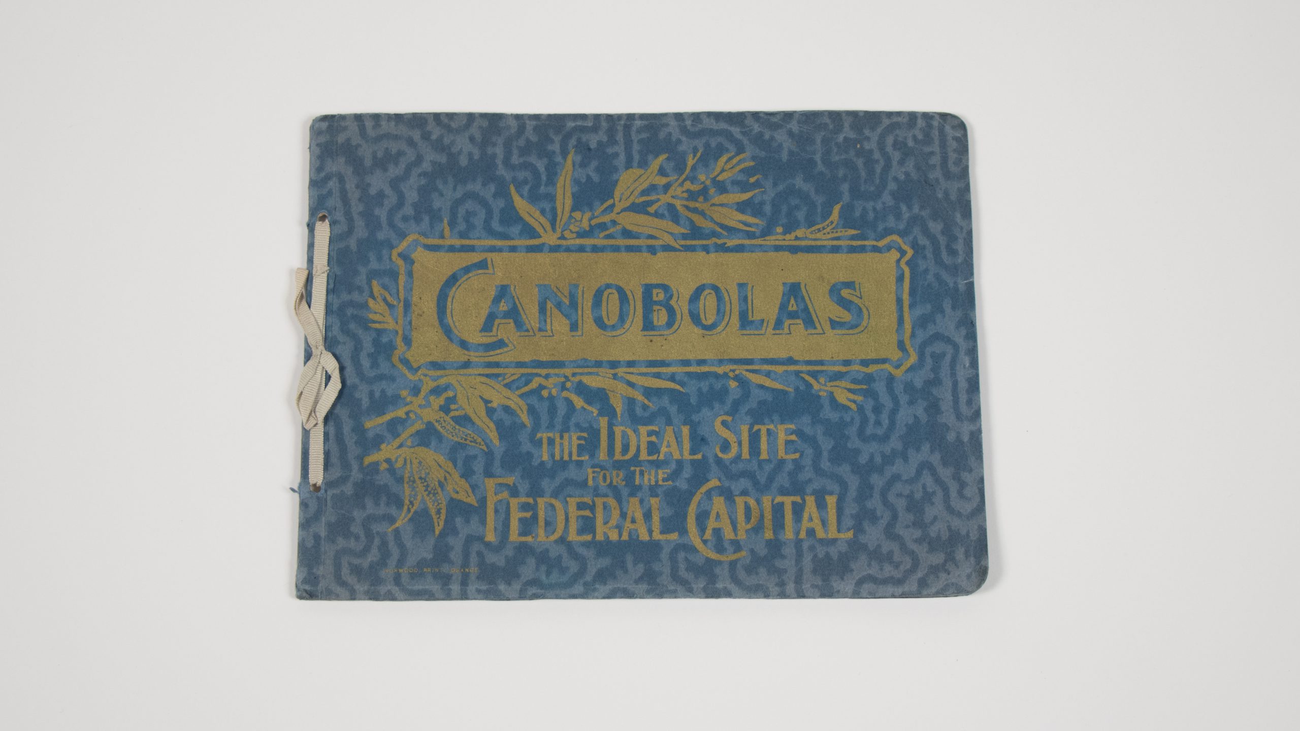 blue booklet bounded with a single string, it has gold lettering and leaf design which reads 'CANOBOLAS / THE IDEAL SITE FOR THE FEDERAL CAPITAL'