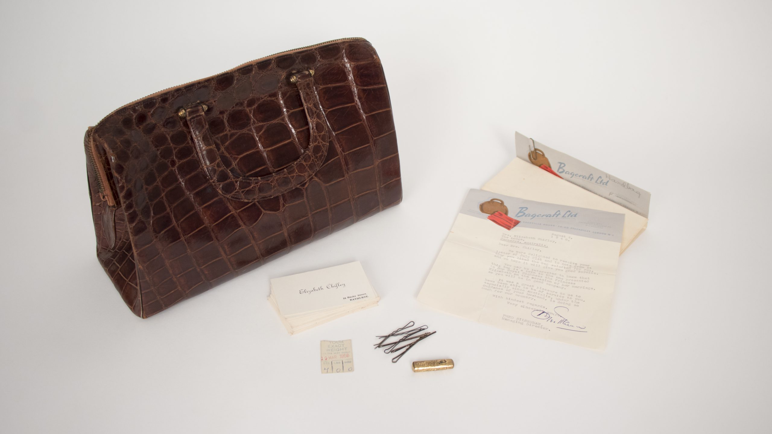 crocodile leather handbag beside two letters, hairpins, a lipstick, and business cards