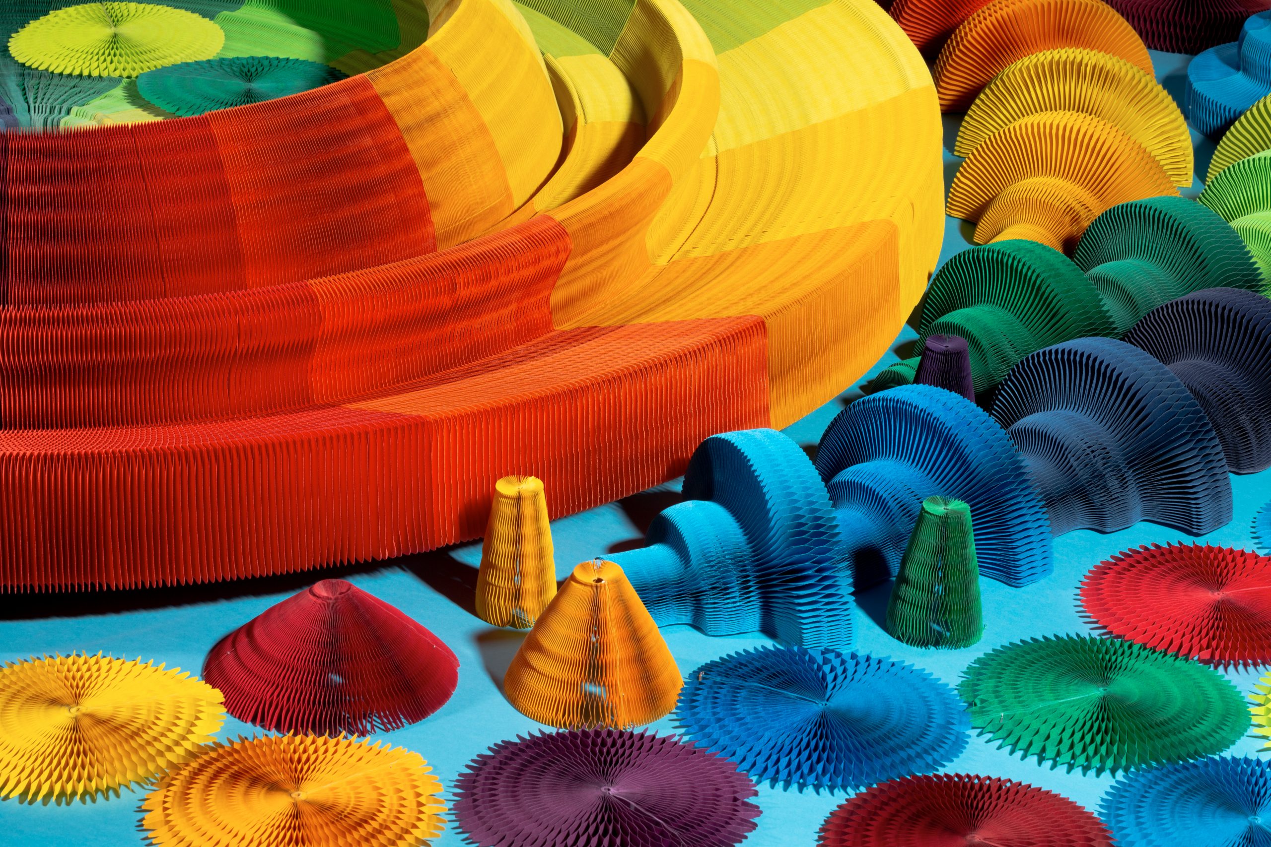 Close up of bright blue room with multi-coloured paper artworks. They are made like paper lanterns, taking the shape of fans despite being made from the shapes of guns